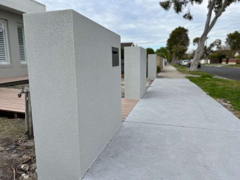 A rendered tall brick fence installed in Golden Beach in front of a wide footpath