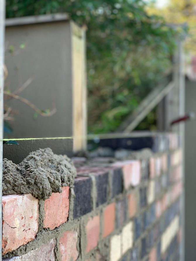 Image of bricks, trowel, mortar, and levelling tool used by Currimundi Bricklayers to install a brick fence in this garden