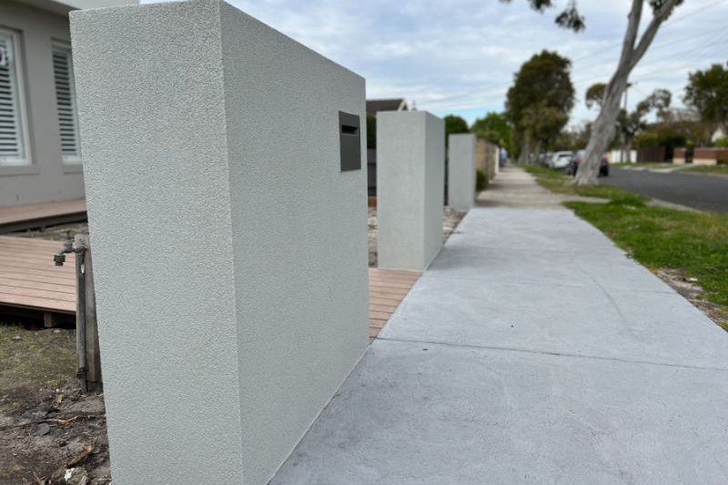 A rendered tall brick fence installed in Golden Beach in front of a wide footpath