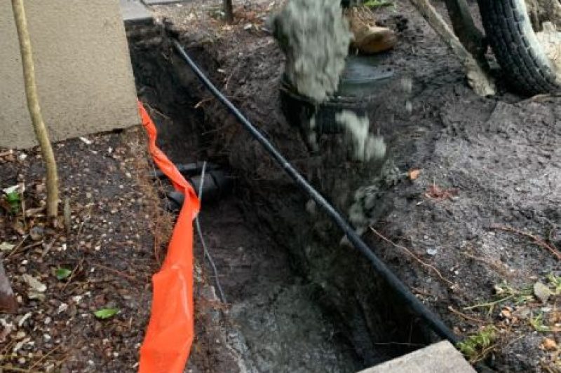 Concrete on a wheelbarrow is being poured into a trench for the concrete footing of this brick fence in Little Mountain