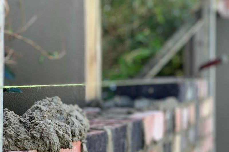 Image of bricks, trowel, mortar, and levelling tool used by Currimundi Bricklayers to install a brick fence in this garden